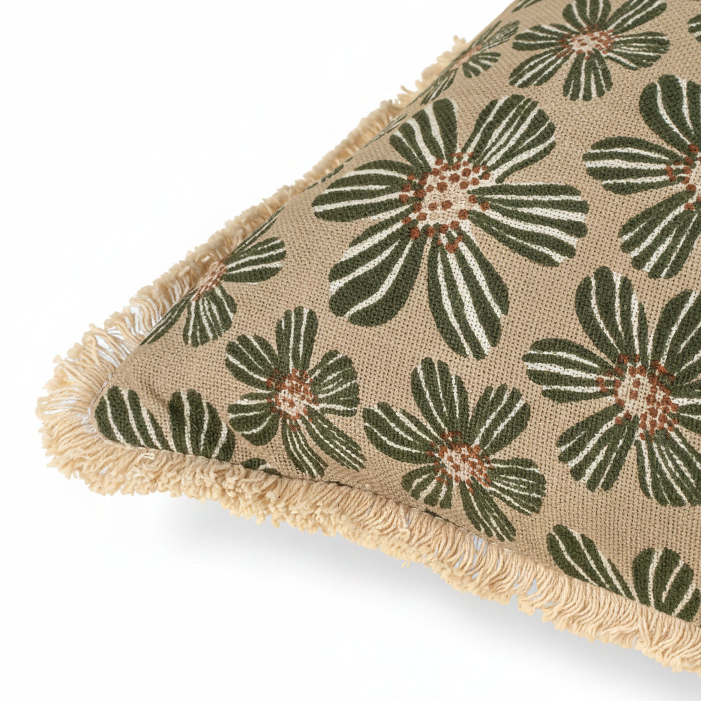A close-up of a decorative throw pillow featuring a woven floral pattern in olive green, cream, and brown on a beige linen-like background, finished with a fringed edge.