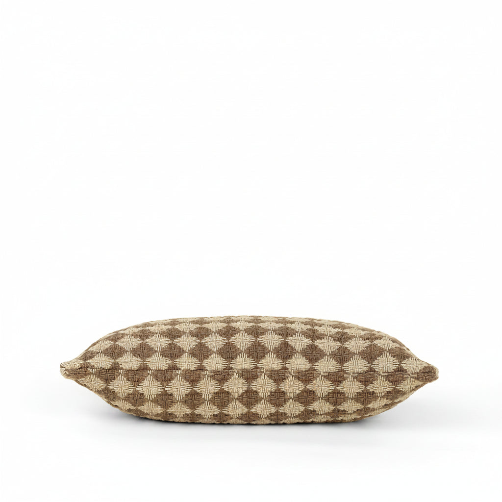 A rectangular throw pillow with a brown and beige geometric diamond pattern, photographed against a solid cream background.