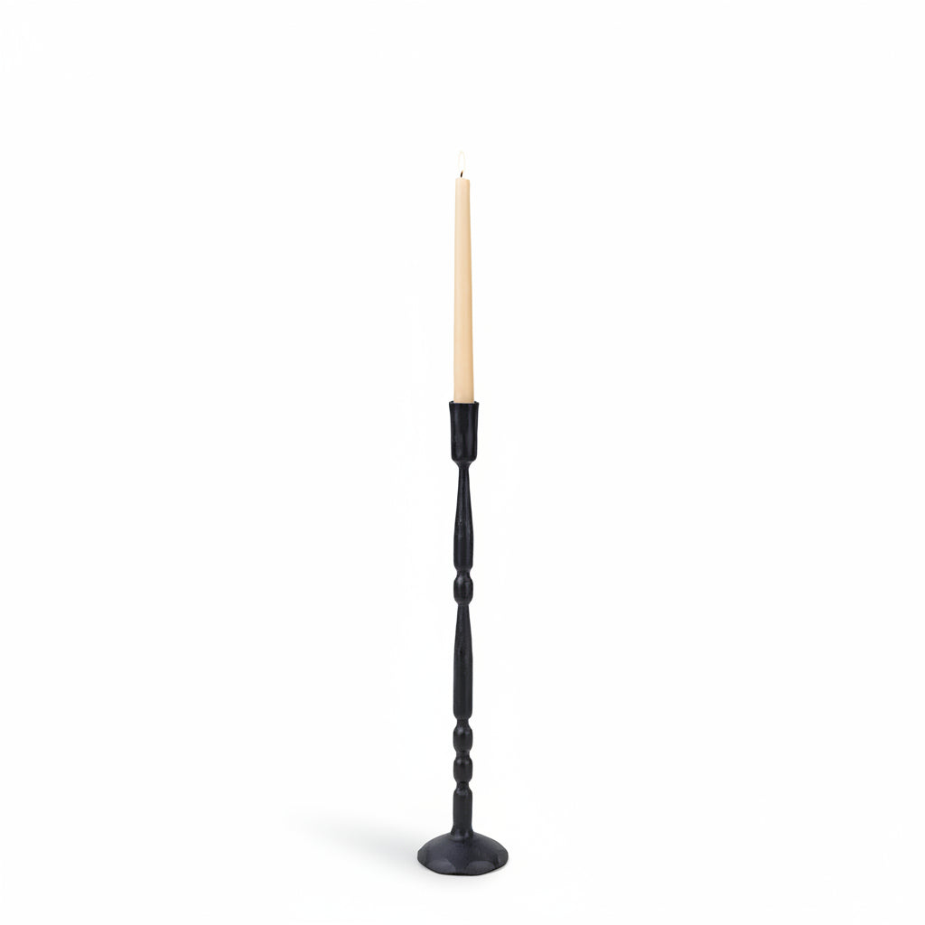 A tall black candlestick holder with a twisted spindle design and a single cream-colored taper candle, set against a solid light beige background.