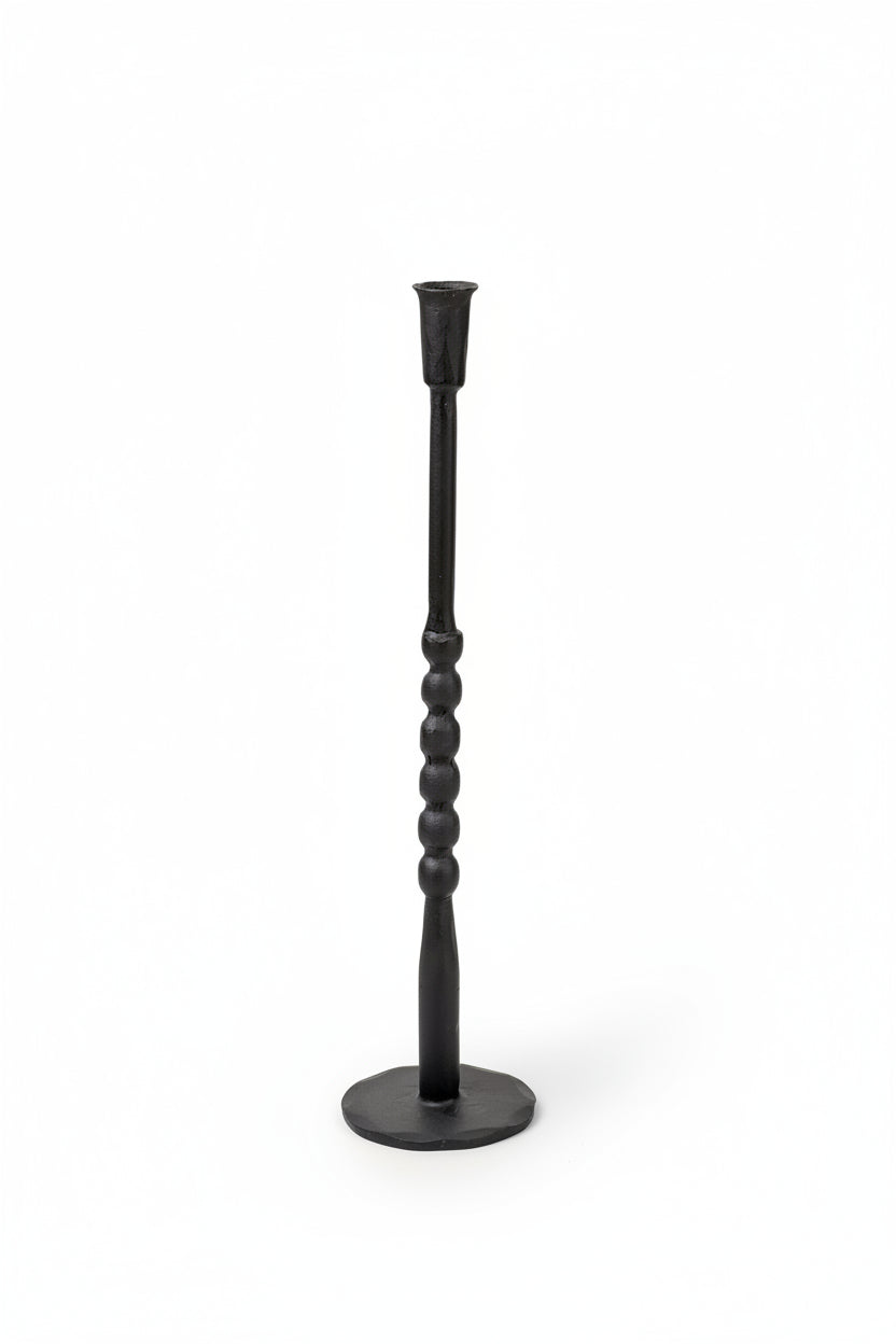 A black metal candlestick holder with a twisted handle design and a round base, shown against a plain cream background.