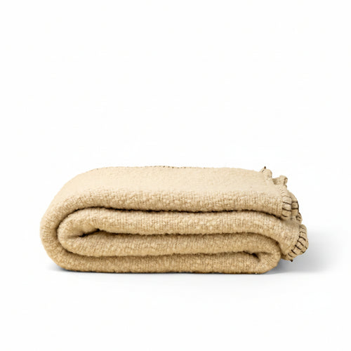 A folded beige textured blanket with fringed edges, photographed on a solid cream background.
