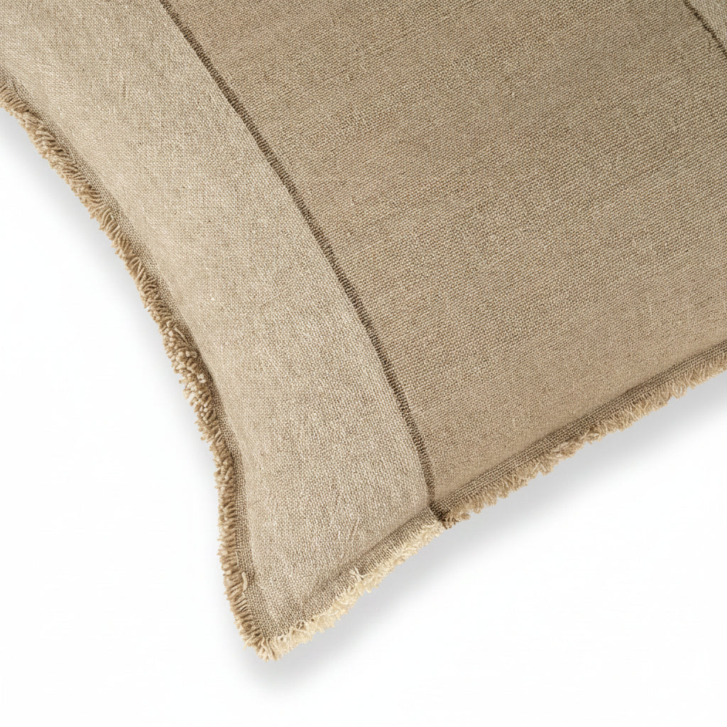 A close-up of a textured woven throw blanket in a warm taupe-beige color, showing its fringed edge against a solid cream background.
